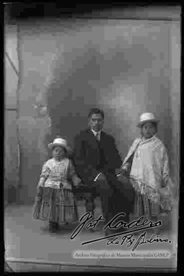 Foto de estudio de una familia: padre junto a sus dos hijas vestidas de cholitas