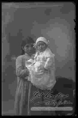 Foto de estudio de un bebe sujetado por una niña de pollera