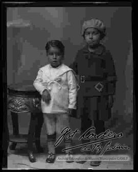 Foto de estudio de un niño y una niña, parados junto a un taburete