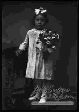 Foto de estudio de una niña parada encima de un sillón, sosteniendo en mano unas flores