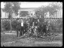 Grupo de varones vestidos de traje, celebrando un acontecimiento, con música y compartiendo bebidas en el jardín de una casa particular