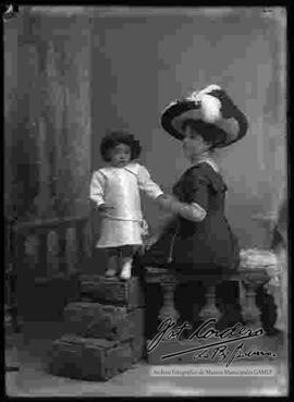 Foto de estudio de una dama junto a su niña, luciendo un sombrero.