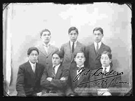 Foto de estudio de un grupo de siete jóvenes vestidos de traje