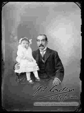 Foto de estudio con esfumador, de un padre sentado en un sillón sosteniendo a su hija pequeña