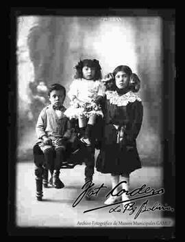 Foto de estudio de tres niños (hermanitos). Dos niñas y un niño sentado en un sillón