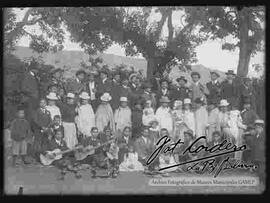 Reunión familiar celebrando el bautizo de niños. en el patio de una casa. donde se puede apreciar a las cholas paceñas usando el sombrero blanco de copa alta