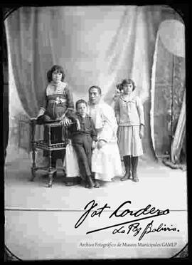 Foto de estudio de tres niños. Dos niñas y un niño junto a un cura