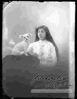 Foto de estudio con esfumador de una señorita parada junto a su perrito, que se encuentra sentado encima de la cabecera de un sillón