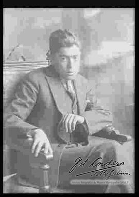 Reproducción de la fotografía de un joven que viste de traje y que se encuentra sentado en una silla.