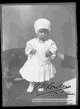 Foto de estudio de una niña pequeña vestida de blanco y parada encima de un sillón
