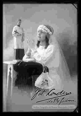 Foto de estudio de una niña junto a una imagen religiosa, en el día de su primera comunión