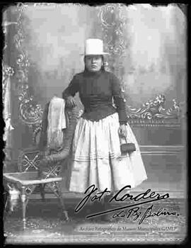 Foto de estudio de una chola con sombrero de copa alta, color blanco, sujetando una escarcela (cartera)