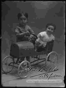 Foto de estudio de un niño junto a su hermanito pequeño que se encuentra en un coche de juguete