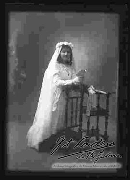 Foto de estudio de la niña Hortensia Burgoa M. del colegio del Buen Pastor, de rodillas sobre una silla,  el día de su primera comunión