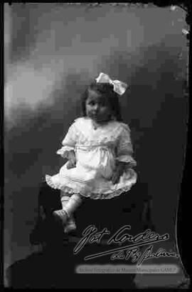 Foto de estudio de una niña que se encuentra sentada en la cabecera de un sillón