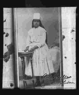 Reproducción de la fotografía de una chola que se encuentra parada junto a un mueble.