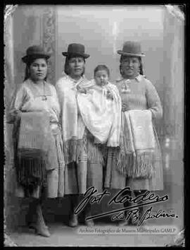 Foto de estudio de tres cholas que llevan puesto sombreros borsalinos. Dos de ellas usan chompas y sostienen en el brazo sus mantas. Otra sostiene a un bebe en mano