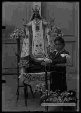 Un niño con ropa de primera comunión junto a la imagen de la Virgen de la Merced.