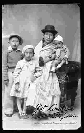 Foto de estudio de una familia. Una chola que se encuentra sentada en un sillón  junto a sus tres hijos