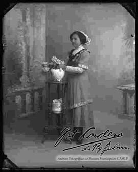 Foto de estudio de una dama tocando las flores de un florero que se encuentra encima de una mesita