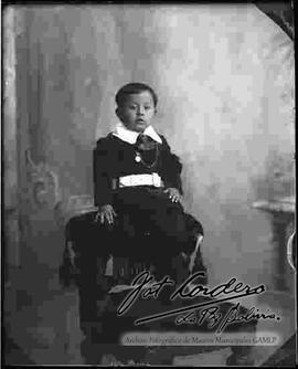 Foto de estudio de un niño pequeño, vestido con uniforme y sentado encima de la cabecera de un sillón