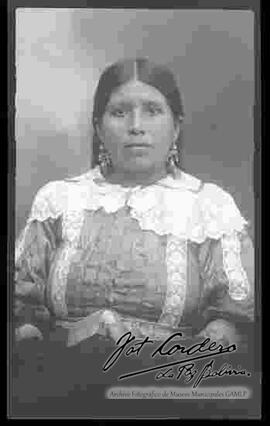 Foto de estudio de medio cuerpo de una chola. Luce una blusa fina de encajes, con aretes y sin sombrero