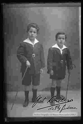 Foto de estudio de dos niños que se encuentran parados y sosteniendo en mano unos bastones