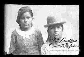 Toma de medio cuerpo de una chola junto a una niña. Lleva puesto un sombrero borsalino, aretes y una blusa