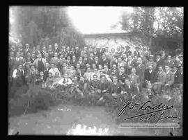 Grupo de varones, reunidos en el patio de una casa, detrás de un charco de agua, por la celebración de carnavales.