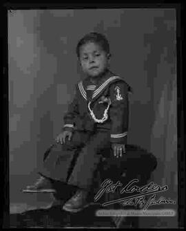 Foto de estudio de un niño vestido de marinero y sentado en la cabecera de un sillón.