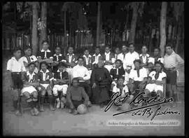 Equipo de futbol de algún colegio, acompañados por un cura, en un parque