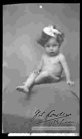 Foto de estudio de una niña pequeña y desnuda que se encuentra sentada sobre una manta