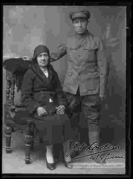 Foto de estudio de un soldado de la Guerra del Chaco junto a su madre, que se encuentra sentada en un sillón