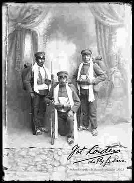 Tres soldados de la expedición al Acre cargando su equipo de campaña, en el patio de un cuartel, con el fondo de estudio