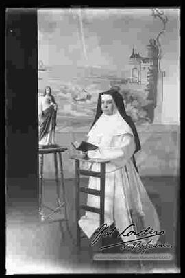 Foto de estudio de una monja, de rodillas en un reclinatorio, junto a la Imagen del Sagrado Corazón de Jesús