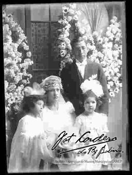 Novios junto a dos niñas, delante de arreglos florales, en el interior de una casa particular, en el día de su matrimonio