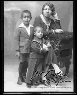 Foto de estudio de una madre sentada en un sillón, junto a sus dos hijos pequeños