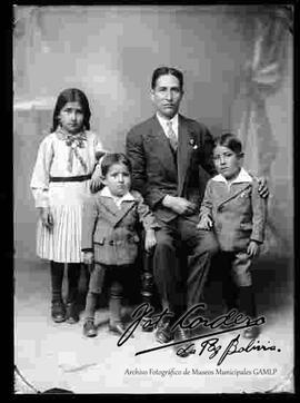 Foto de estudio de un padre sentado en un sillón junto a sus tres hijos