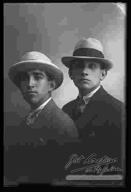 Foto de estudio de  dos jóvenes de medio cuerpo, luciendo trajes con corbata y sombrero.