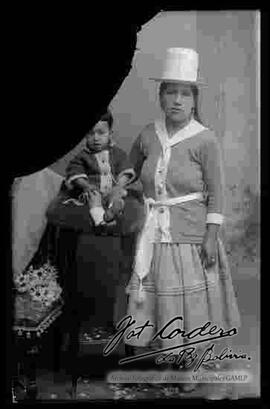 Foto de estudio de una chola junto a un bebe que se encuentra sentado encima de una mesita.