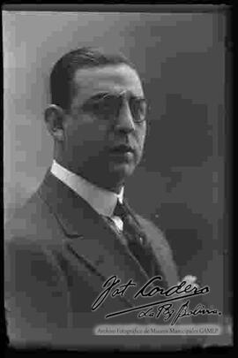 Foto de estudio de medio cuerpo de un varón de lentes, traje y corbata