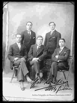 Foto de estudio de cinco jóvenes vestidos de traje. Tres se encuentran sentados en sillas y dos parados por detrás