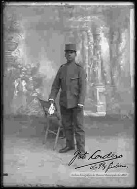 Foto de estudio de un soldado parado junto a una silla, sosteniendo en mano unos guantes blancos