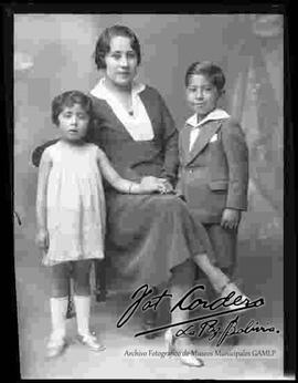 Foto de estudio de una madre sentada en un sillón, junto a sus dos hijos pequeños