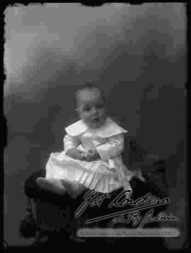 Foto de estudio de una bebe que se encuentra sentada encima de la cabecera de un sillón