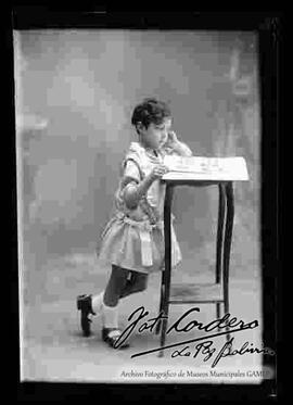 Foto de estudio de una niña apoyada a una mesita, observando un libro