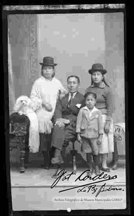 Foto de estudio de una familia, junto a su mascota: Un perrito que se encuentra sentado en la cabecera de un sillón, encima de una manta