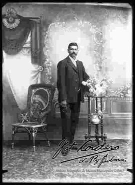 Foto de estudio de un varón que se encuentra sentado y que viste de traje