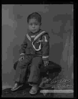 Foto de estudio de un niño vestido de marinero y sentado en la cabecera de un sillón.