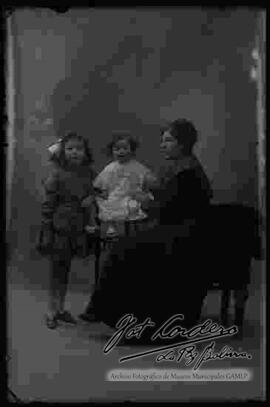 Foto de estudio de una familia. Una madre sentada en un sillón, junto a sus dos hijas pequeñas